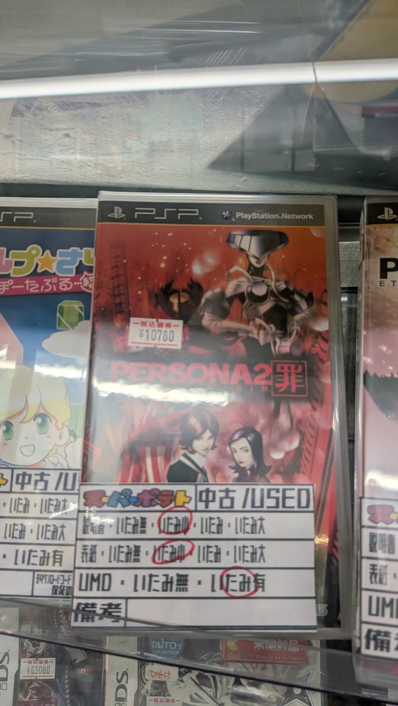 Boxed PSP copy of Persona 2: Innocent Sin (PERSONA2 罪) in a glass display case at Super Potato, with a &yen;10,780 tax-included price tag and a Super Potato used-condition grading card