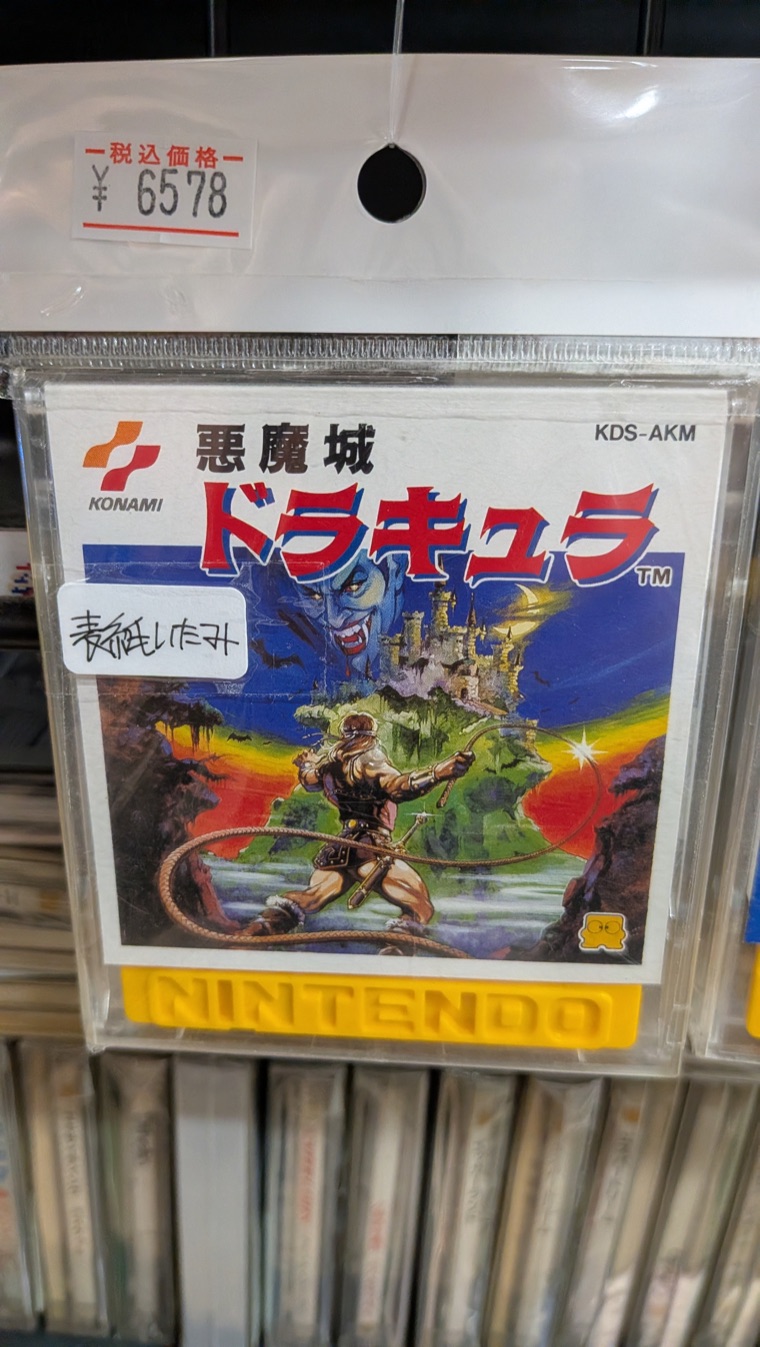 The disk label of the 1986 Famicom Disk System release of 悪魔城ドラキュラ, seen through its clear case, with the product code KDS-AKM printed at the top right
