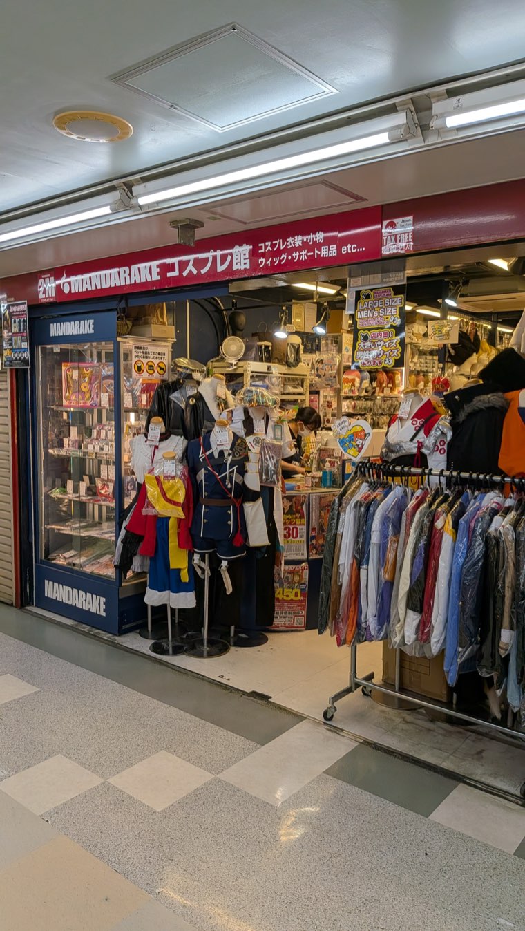 Ladenfront von Mandarake Cosplay-kan mit einem Rollständer voller Kostüme davor und Schaufensterpuppen im Eingang