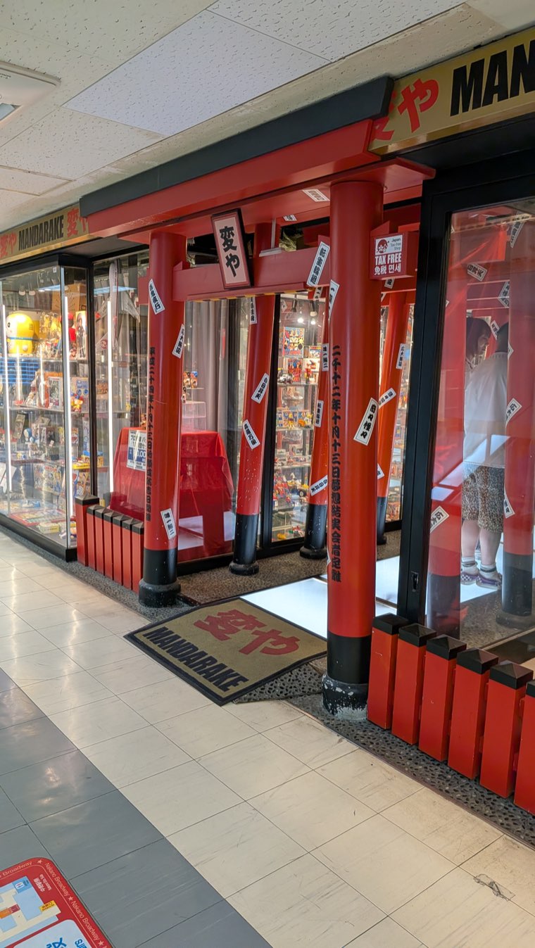 Ladenfront von Mandarake Hen-ya im 4. Stock, als rotes Schreintor mit hängenden Papierstreifen gebaut, daneben Vitrinen mit Spielzeug