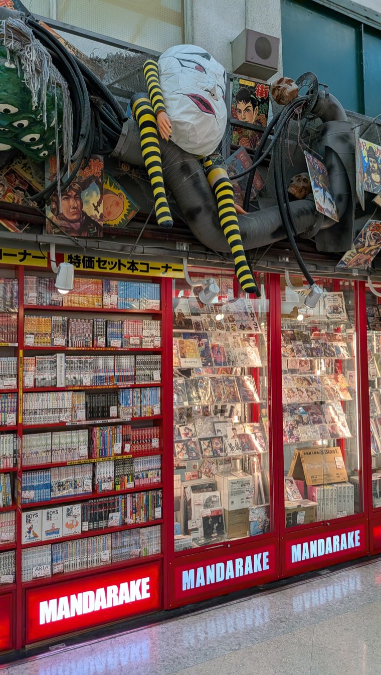 Ladenfront des Mandarake Hauptgeschäfts im 3. Stock, Wände voller Manga-Bände mit einer überlebensgroßen Figur über den Regalen