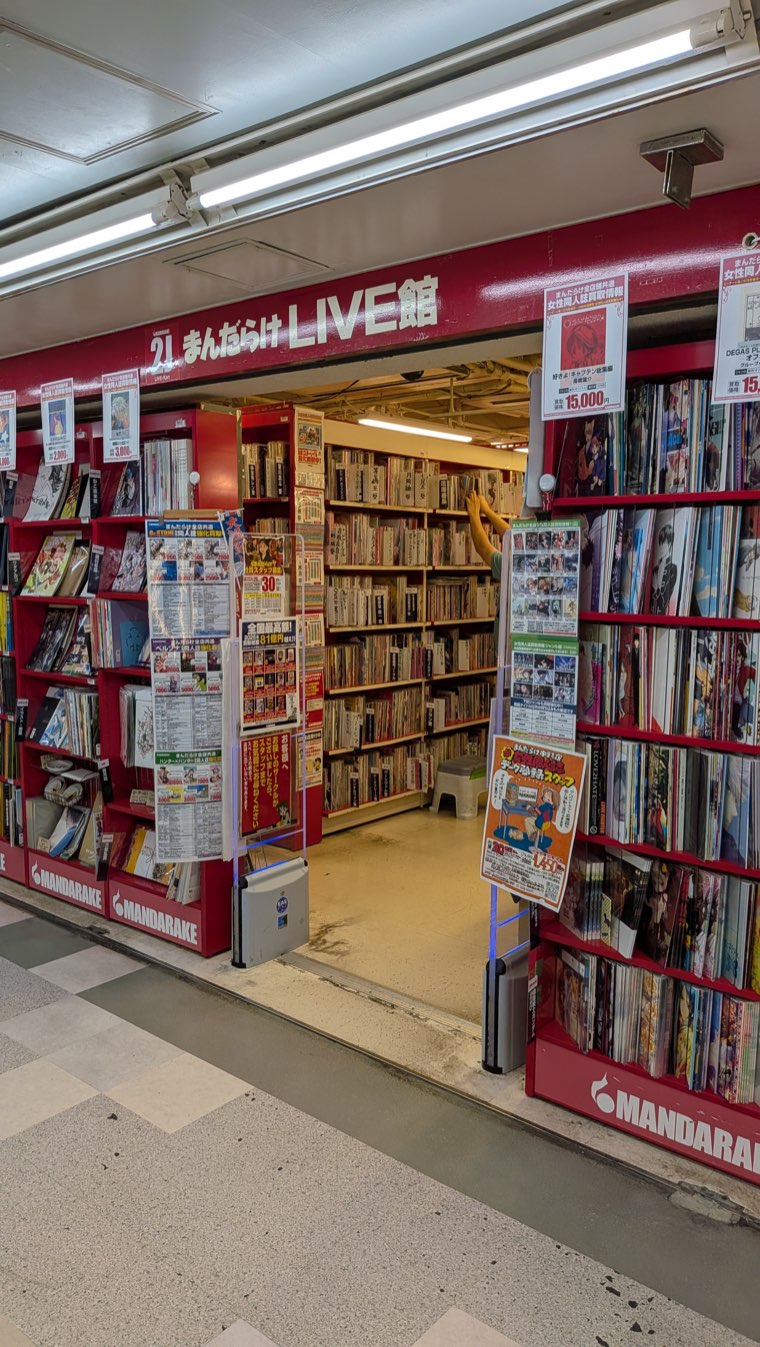 Rote Ladenfront von Mandarake LIVE-kan, durch den Eingang sind tiefe Gänge mit Doujinshi-Regalen zu sehen