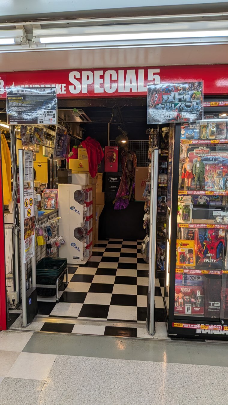Ladenfront von Mandarake Special 5 mit schwarz-weißem Schachbrettboden und amerikanischen Actionfiguren auf Blisterkarten in den Vitrinen